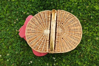 Photo of One picnic wicker basket with checkered napkin on green grass, top view