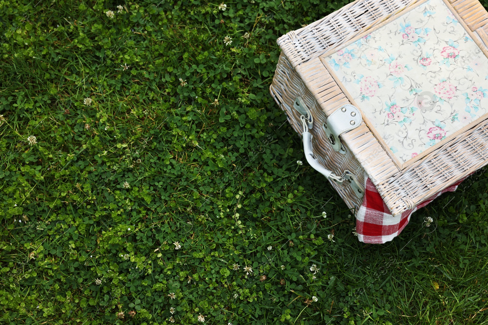 Photo of One picnic wicker basket with checkered napkin on green grass, above view. Space for text