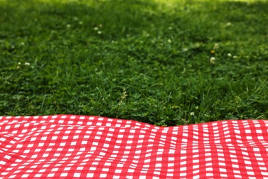 Photo of Checkered picnic tablecloth on green grass, closeup. Space for text