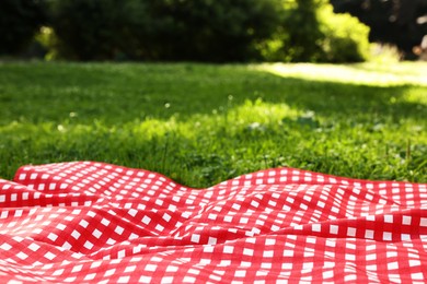 Photo of Checkered picnic tablecloth on green grass, closeup. Space for text