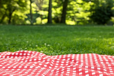 Photo of Checkered picnic tablecloth on green grass, closeup. Space for text