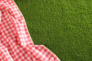 Photo of Checkered picnic tablecloth on green grass, top view. Space for text