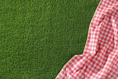 Photo of Checkered picnic tablecloth on green grass, top view. Space for text