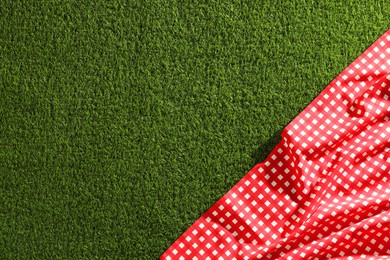 Photo of Checkered picnic tablecloth on green grass, top view. Space for text