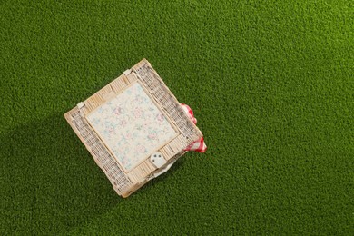 Photo of One picnic wicker basket with checkered napkin on green grass, top view. Space for text