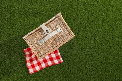 One picnic wicker basket with checkered napkin on green grass, top view. Space for text