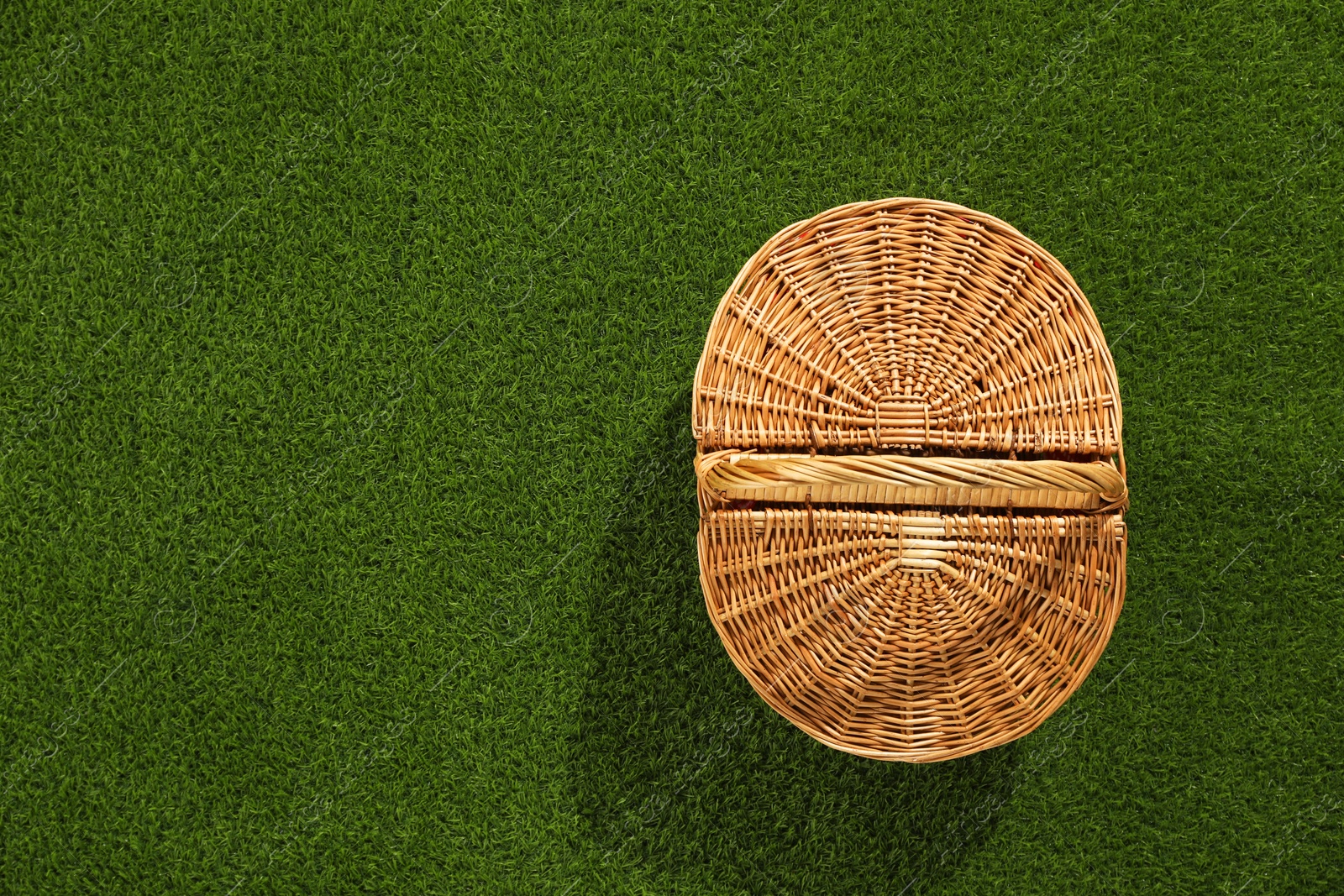 Photo of One picnic wicker basket on green grass, top view. Space for text