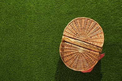 Photo of One picnic wicker basket with checkered napkin on green grass, top view. Space for text