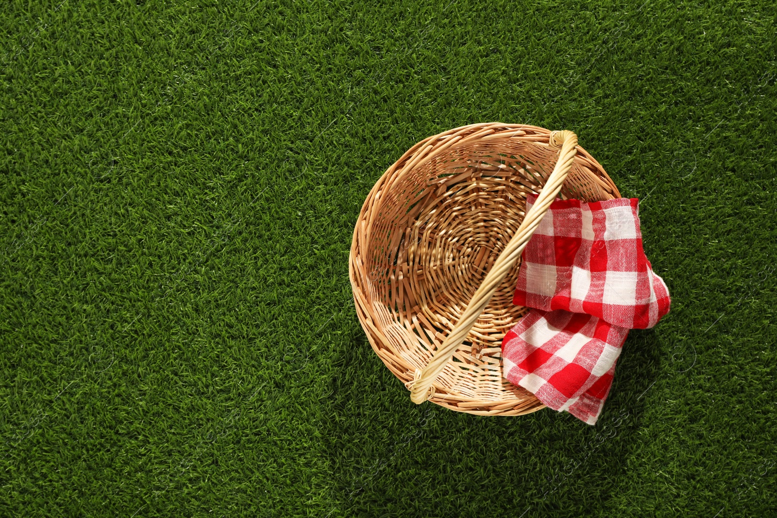 Photo of One picnic wicker basket with checkered napkin on green grass, top view. Space for text