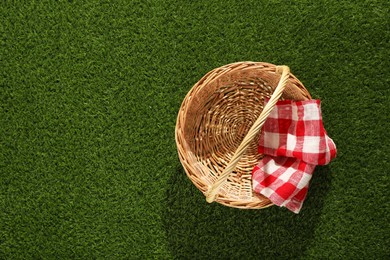 Photo of One picnic wicker basket with checkered napkin on green grass, top view. Space for text