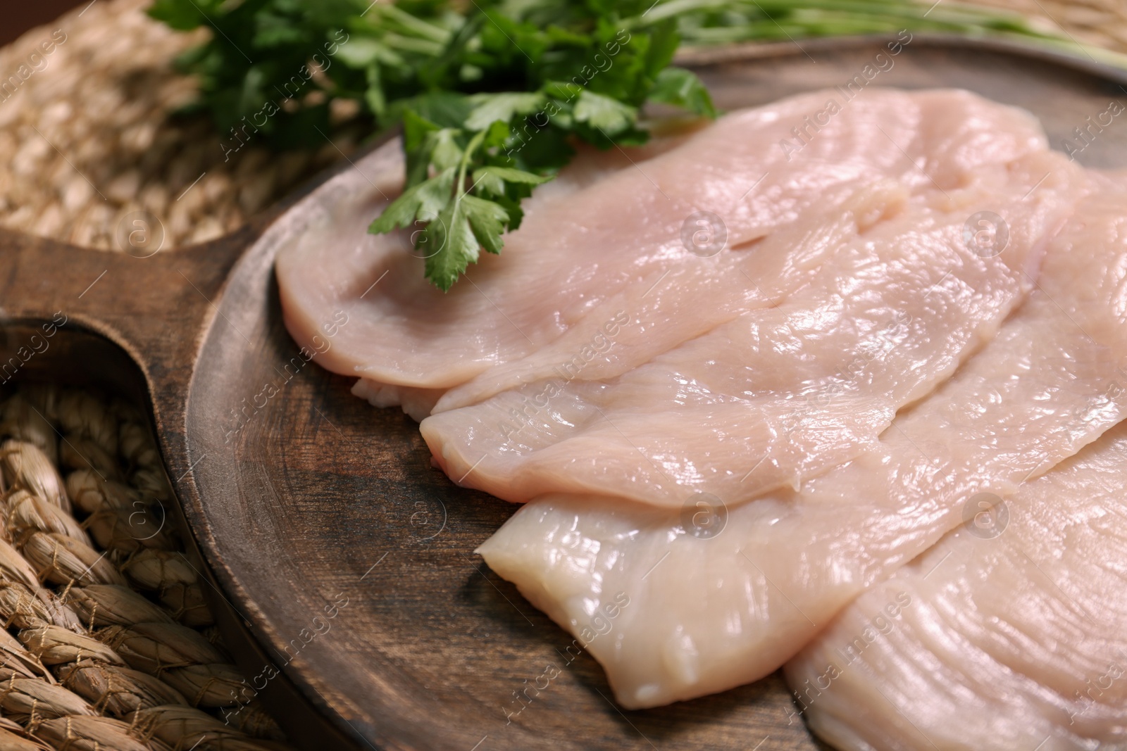 Photo of Making schnitzel. Board with raw meat and parsley on wicker mat, closeup