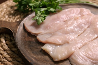 Making schnitzel. Board with raw meat and parsley on wicker mat, closeup