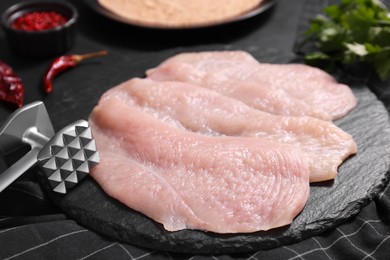 Making schnitzel. Raw meat chops and tenderizer on dark textured table, closeup