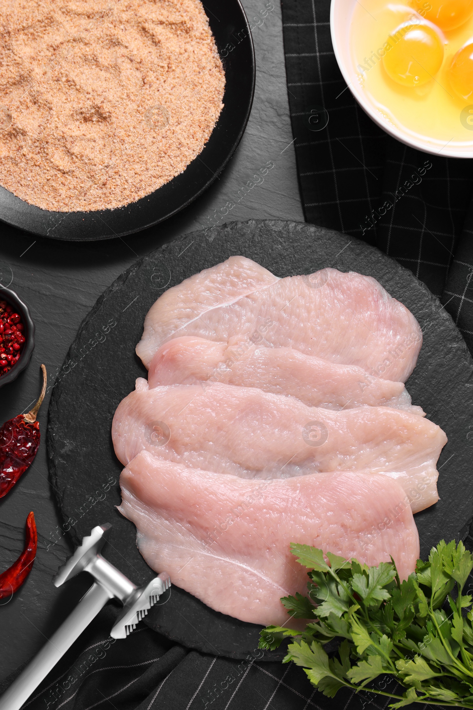 Photo of Making schnitzel. Raw meat chops, products and tenderizer on dark textured table, flat lay