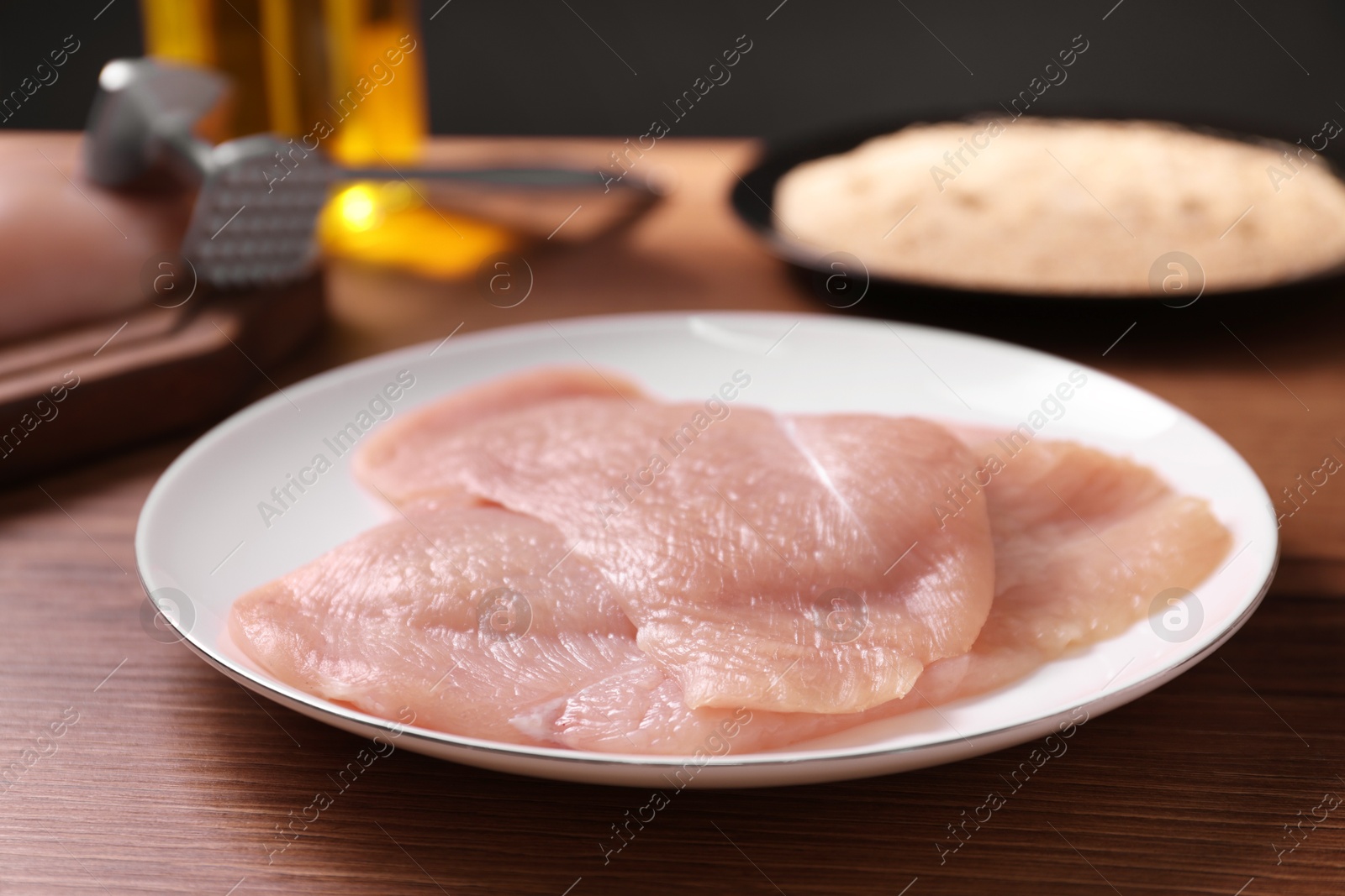 Photo of Making schnitzel. Plate with raw meat on wooden table, closeup