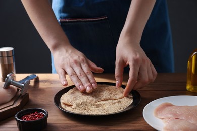 Photo of Making schnitzel. Woman coating slice of meat with bread crumbs at wooden table, closeup