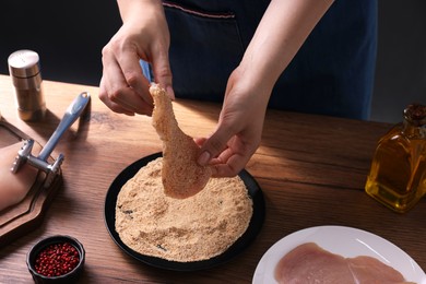 Making schnitzel. Woman coating slice of meat with bread crumbs at wooden table, closeup