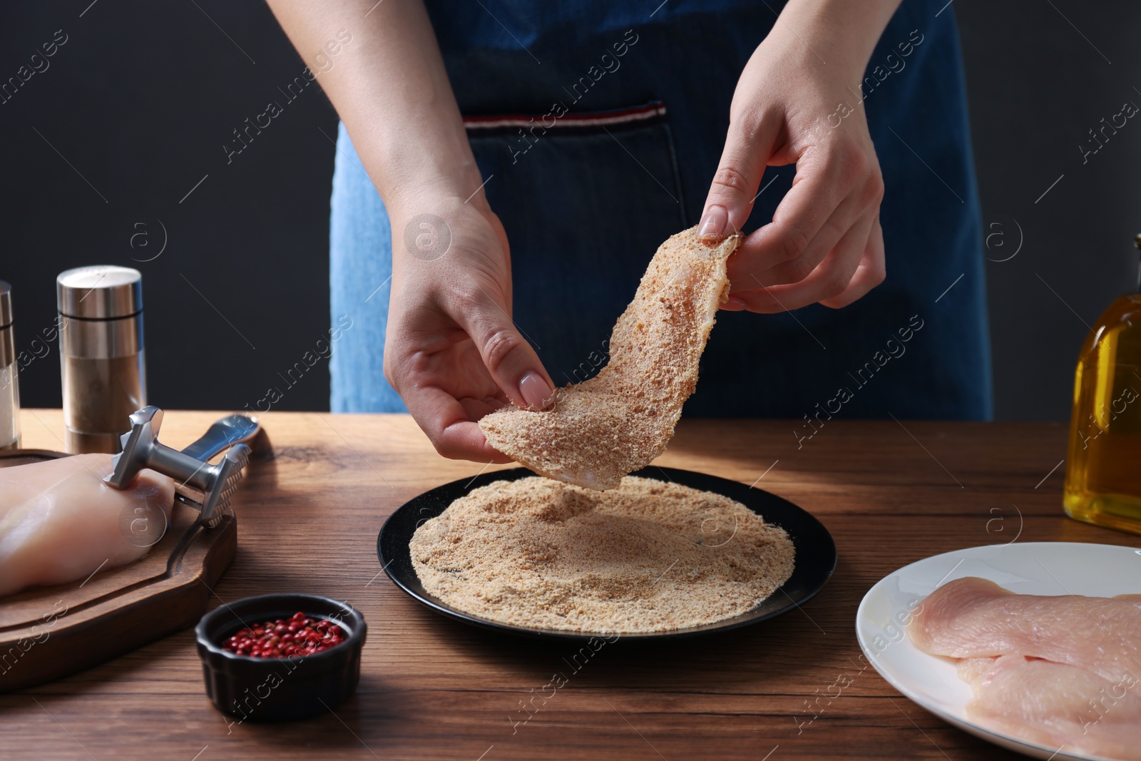 Photo of Making schnitzel. Woman coating slice of meat with bread crumbs at wooden table, closeup