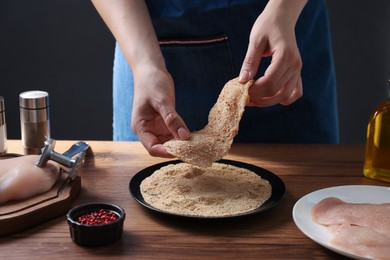 Making schnitzel. Woman coating slice of meat with bread crumbs at wooden table, closeup