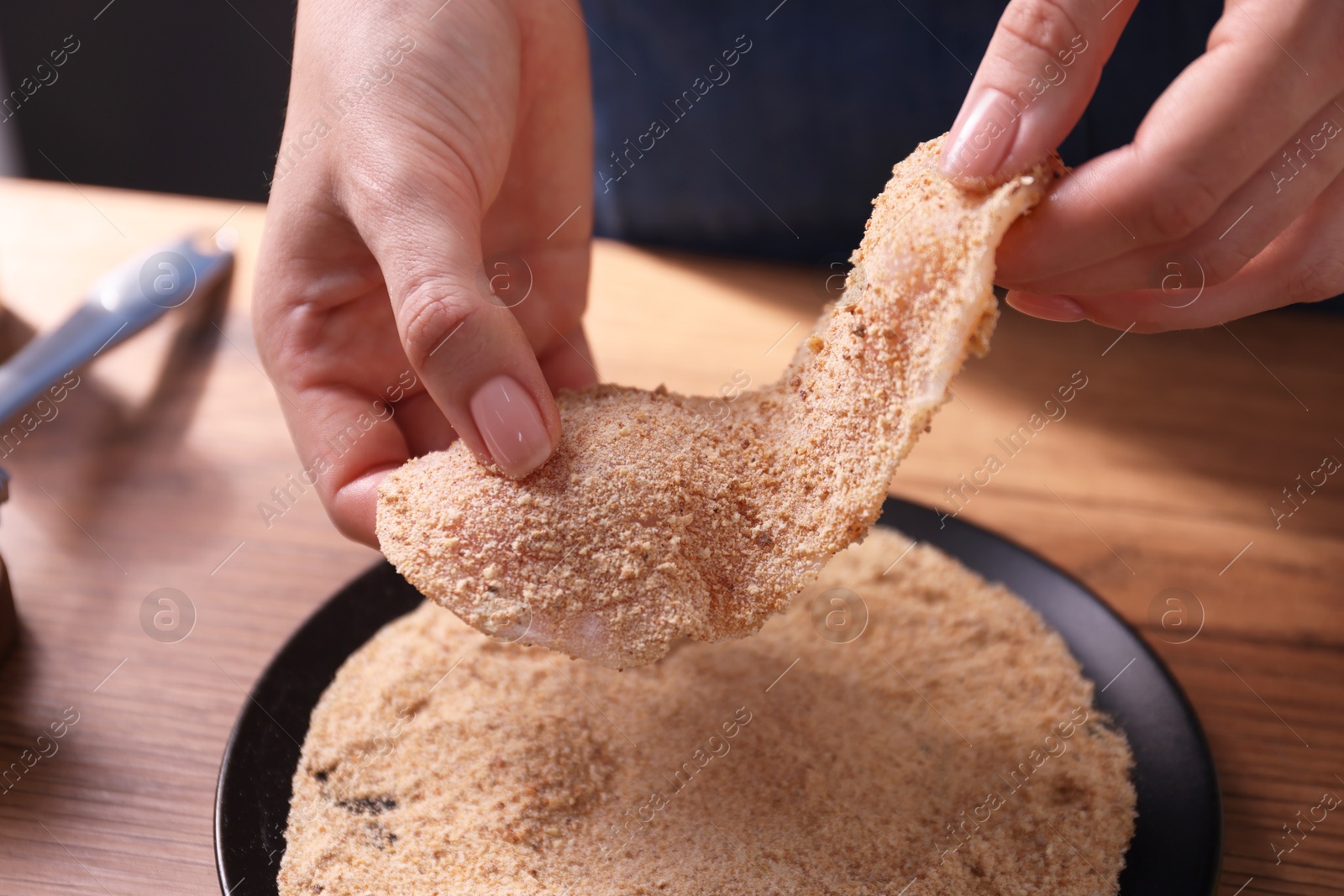 Photo of Making schnitzel. Woman coating slice of meat with bread crumbs at wooden table, closeup