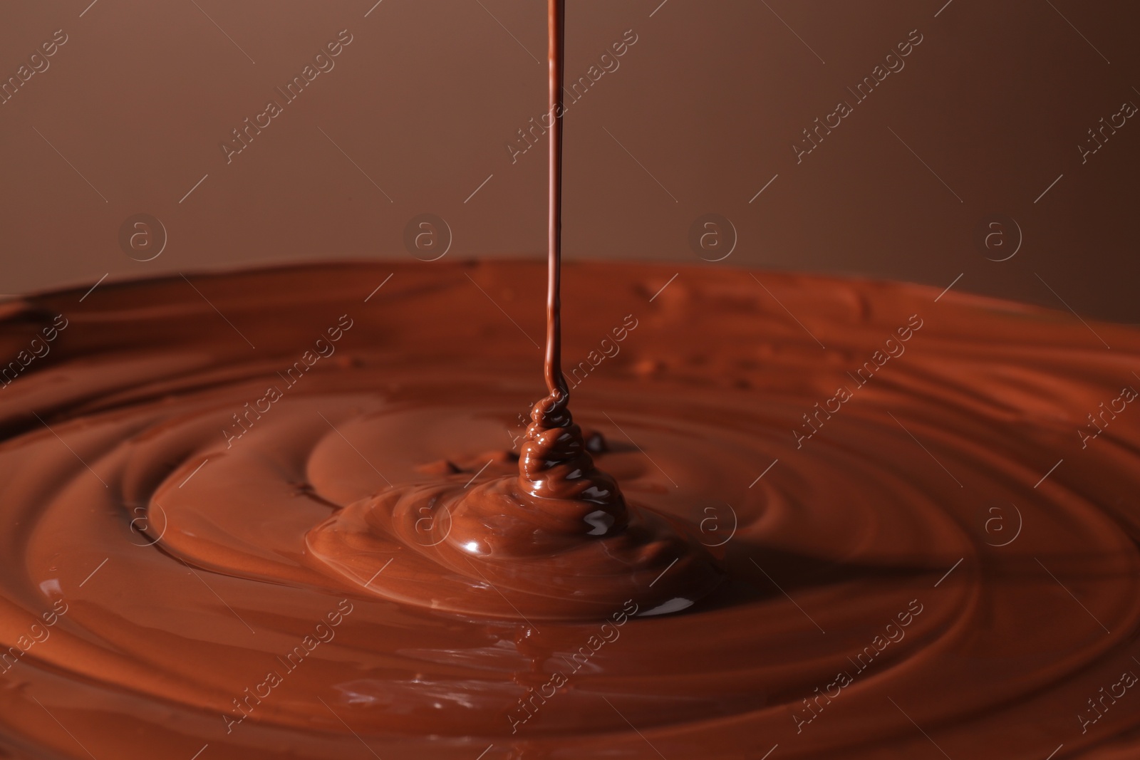 Photo of Pouring delicious melted chocolate on brown background, closeup