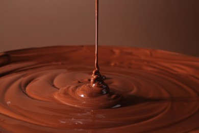 Photo of Pouring delicious melted chocolate on brown background, closeup