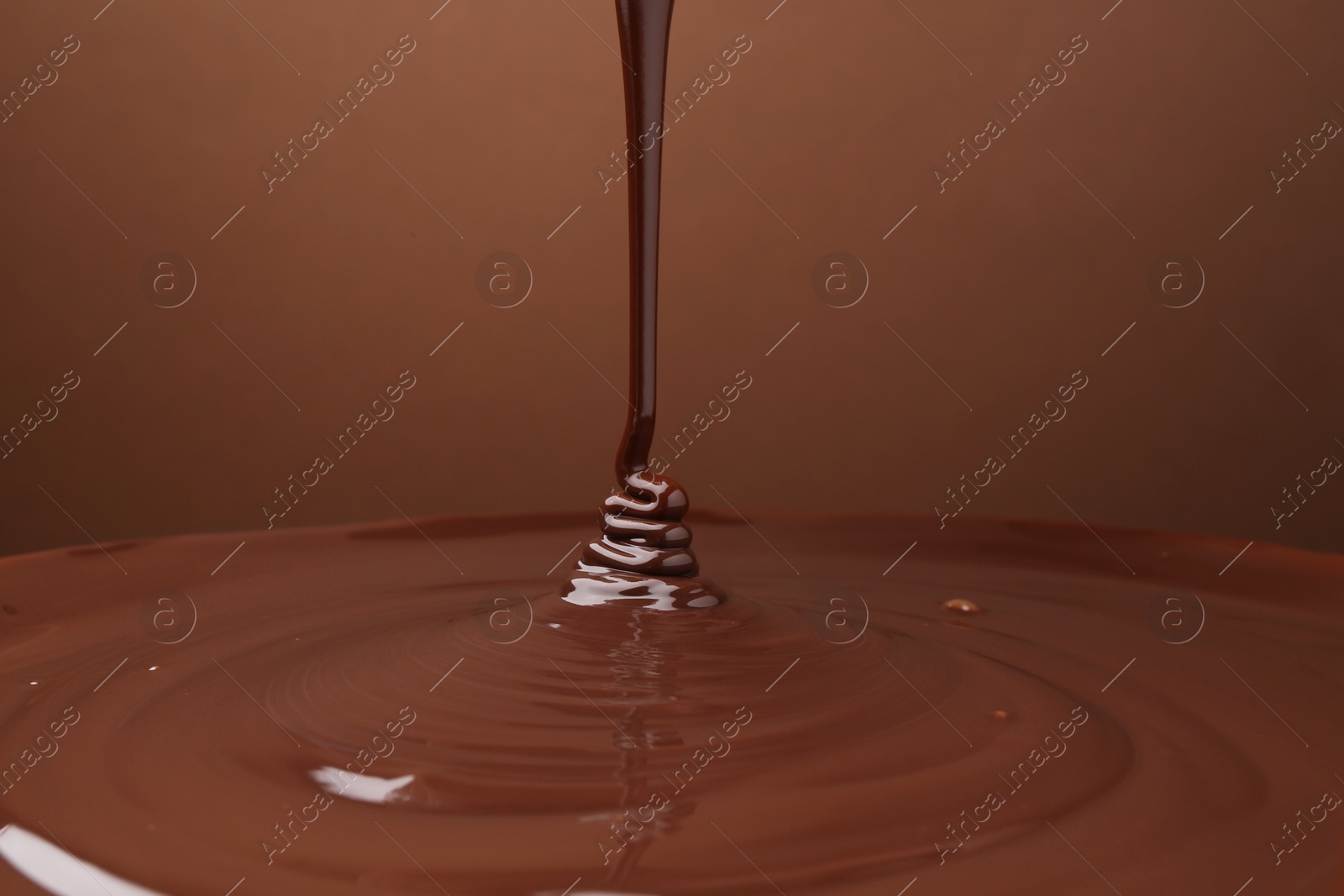 Photo of Pouring delicious melted chocolate on brown background, closeup