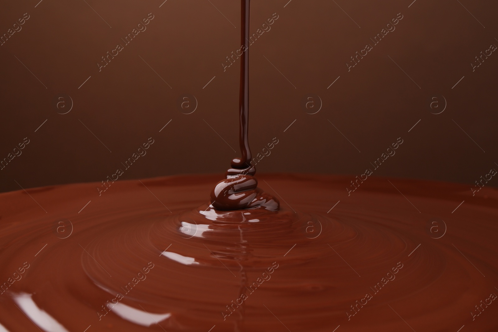 Photo of Pouring delicious melted chocolate on brown background, closeup