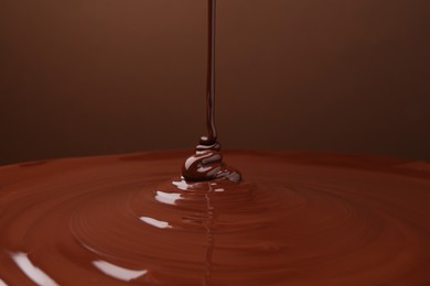 Pouring delicious melted chocolate on brown background, closeup