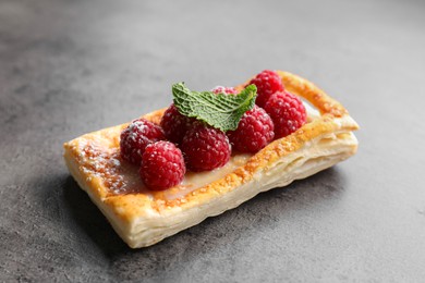 Photo of Tasty puff pastry with raspberries and mint on grey table, closeup