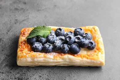 Photo of Tasty puff pastry with blueberries and mint on grey table, closeup