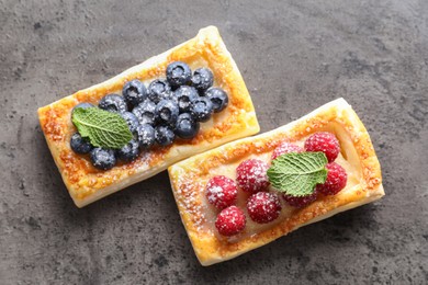 Photo of Tasty puff pastries with berries and powdered sugar on grey table, flat lay