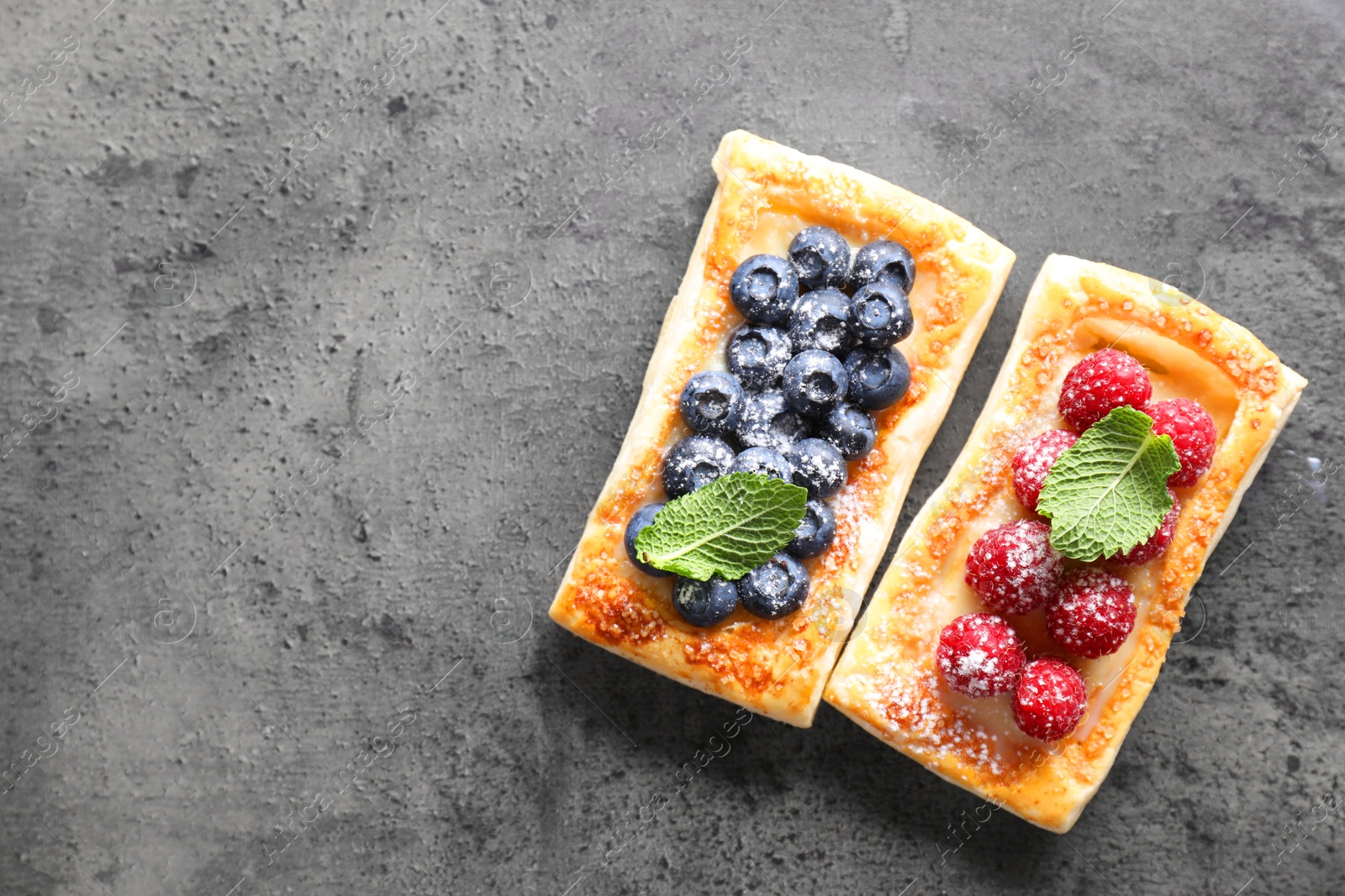 Photo of Tasty puff pastries with berries and powdered sugar on grey table, flat lay. Space for text