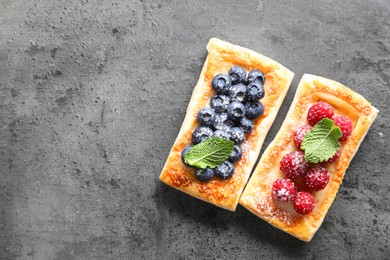 Tasty puff pastries with berries and powdered sugar on grey table, flat lay. Space for text