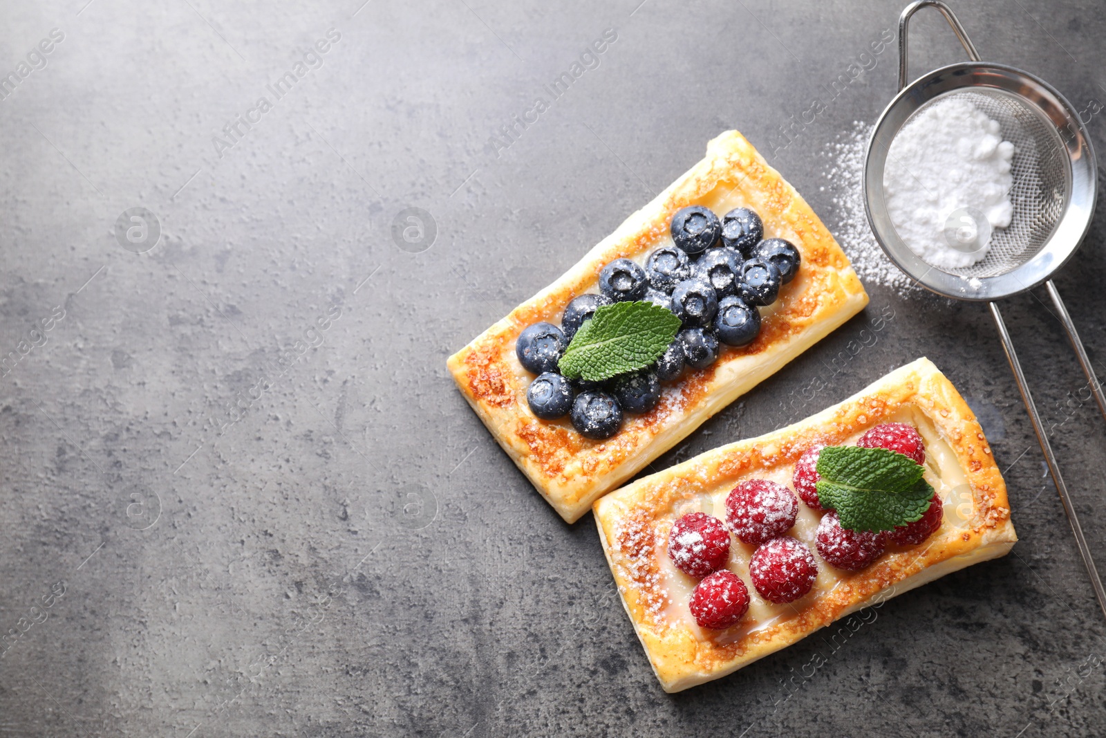 Photo of Tasty puff pastries with berries and powdered sugar on grey table, flat lay. Space for text