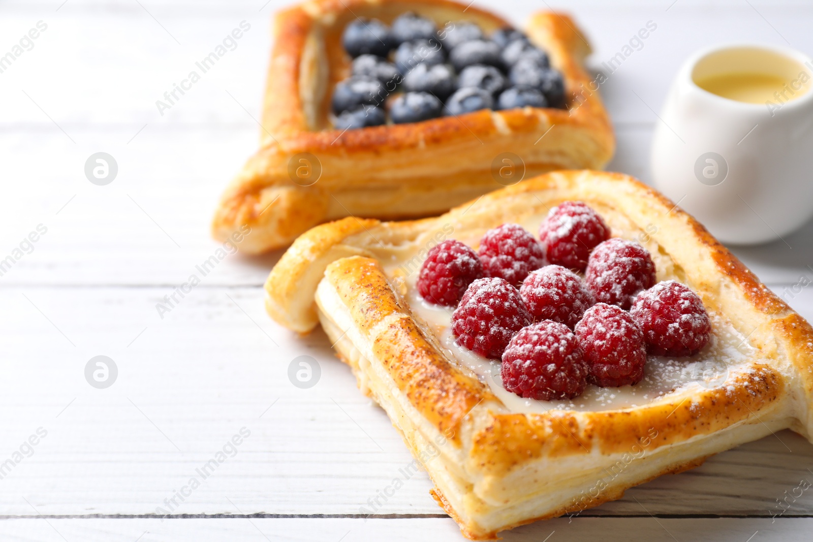 Photo of Tasty puff pastries with berries on white wooden table, closeup