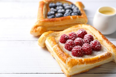 Photo of Tasty puff pastries with berries on white wooden table, closeup