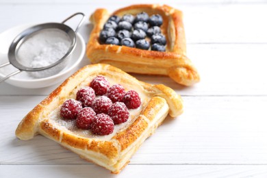 Tasty puff pastries with berries on white wooden table, closeup