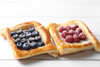 Tasty puff pastries with berries on white wooden table