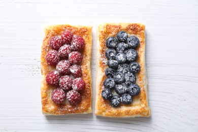 Tasty puff pastries with berries on white wooden table, flat lay