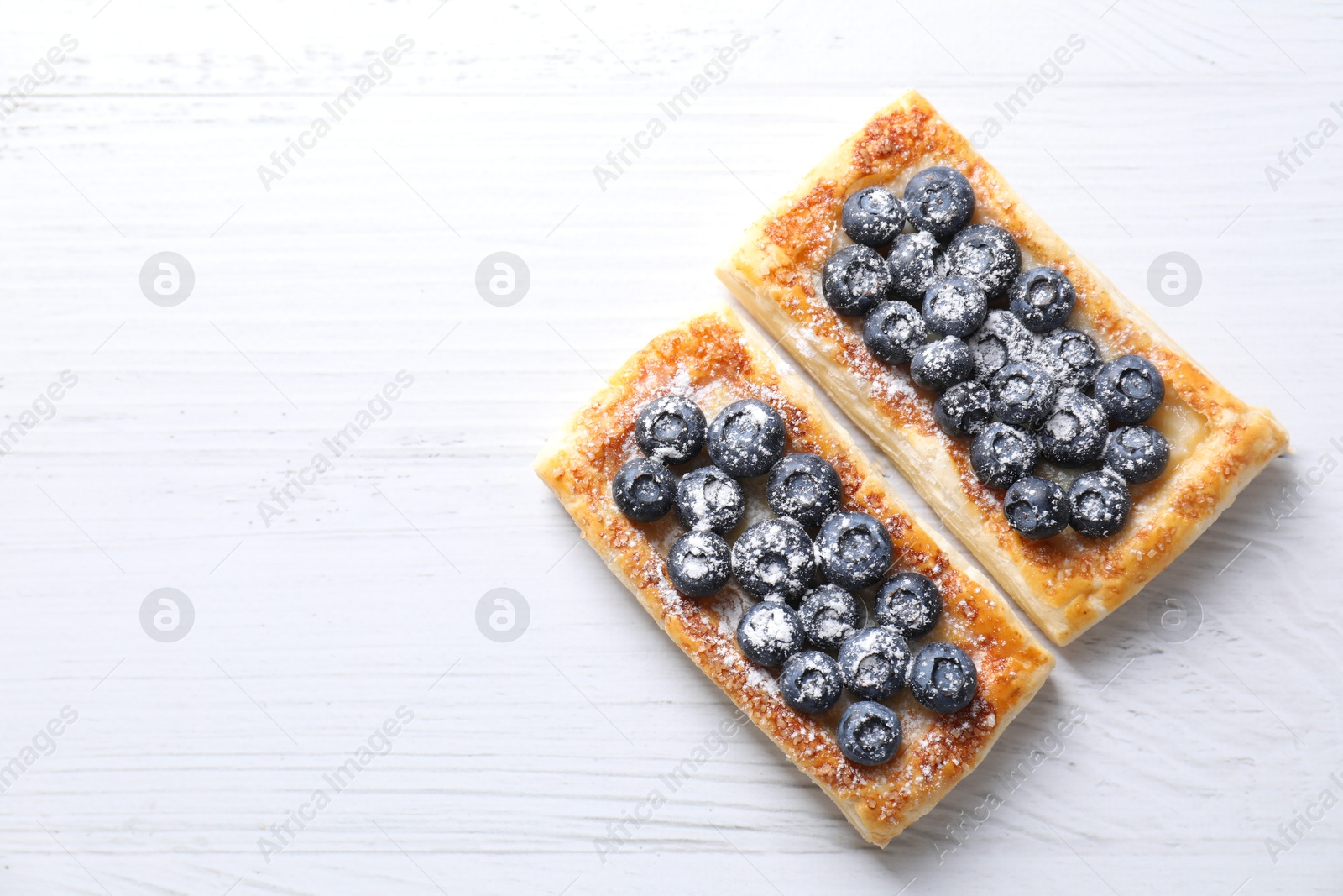 Photo of Tasty puff pastries with blueberries on white wooden table, flat lay. Space for text