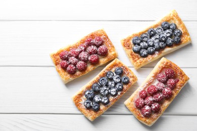 Photo of Tasty puff pastries with berries on white wooden table, flat lay. Space for text