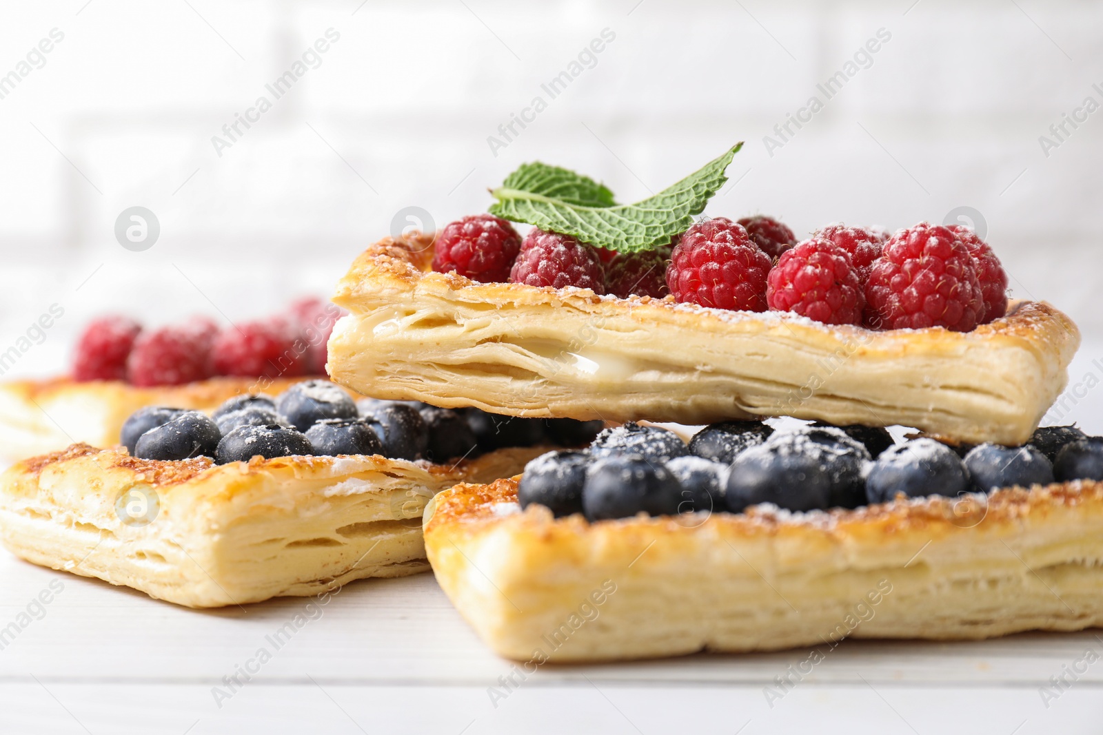 Photo of Tasty puff pastries with berries on white wooden table, closeup