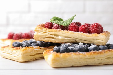 Photo of Tasty puff pastries with berries on white wooden table, closeup