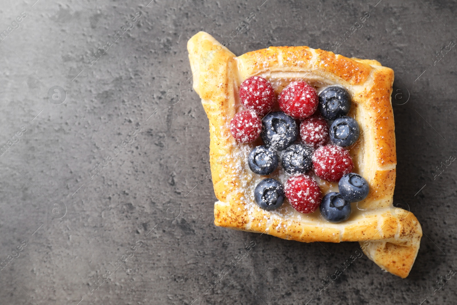 Photo of Tasty puff pastry with berries on grey table, top view. Space for text