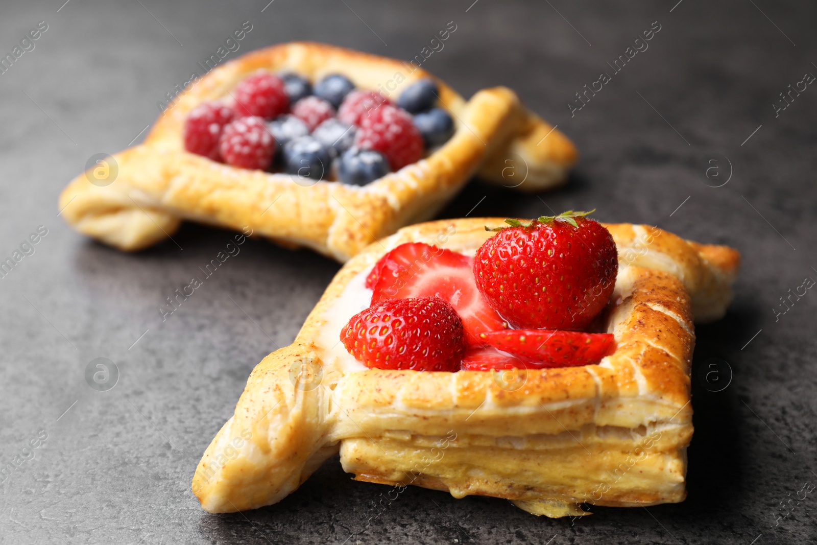 Photo of Tasty puff pastries with berries on grey table, closeup