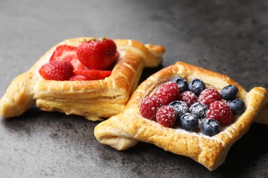 Tasty puff pastries with berries on grey table, closeup