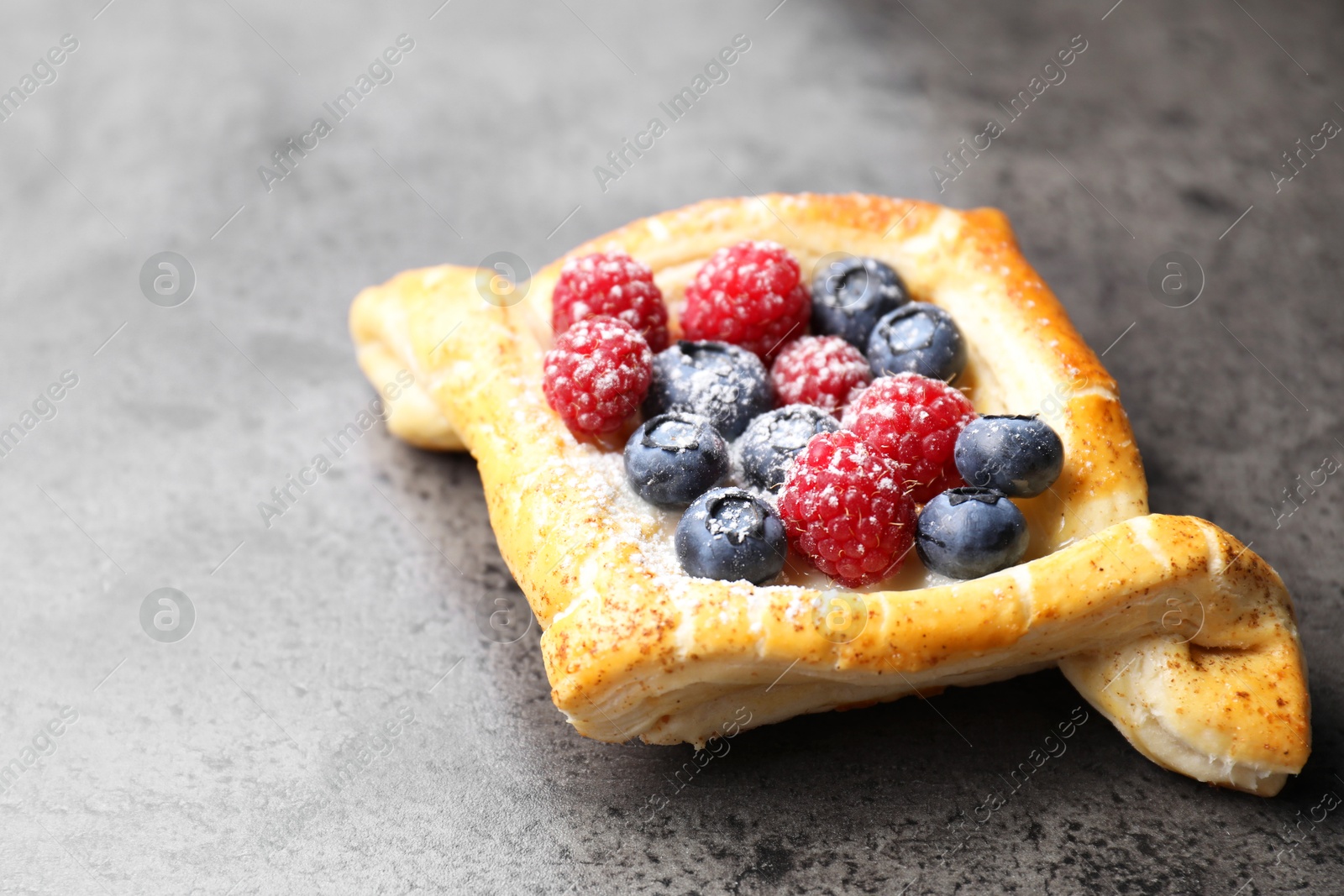 Photo of Tasty puff pastry with berries on grey table, closeup. Space for text