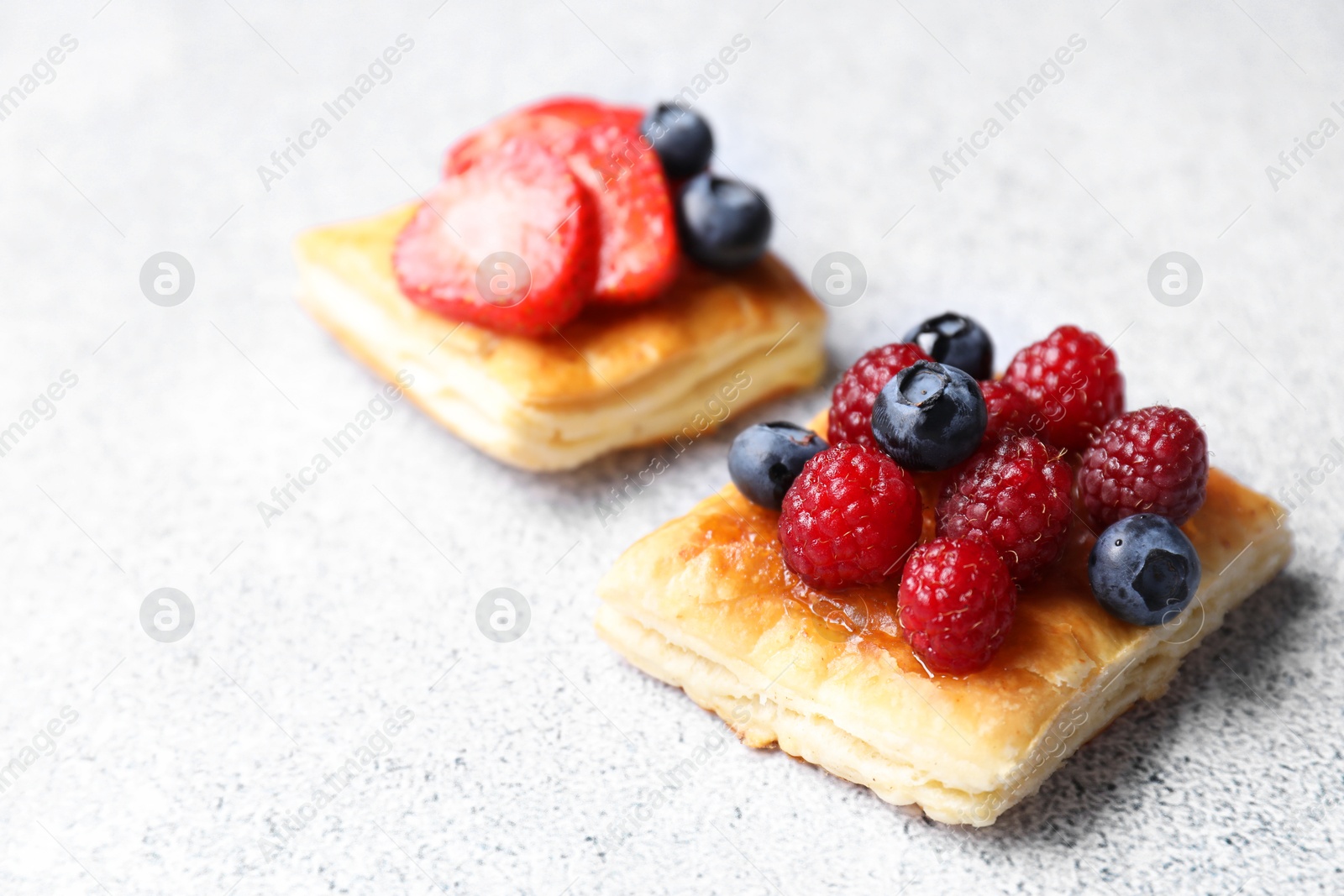 Photo of Tasty puff pastries with berries on light grey table, closeup. Space for text