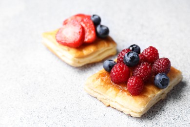 Photo of Tasty puff pastries with berries on light grey table, closeup. Space for text